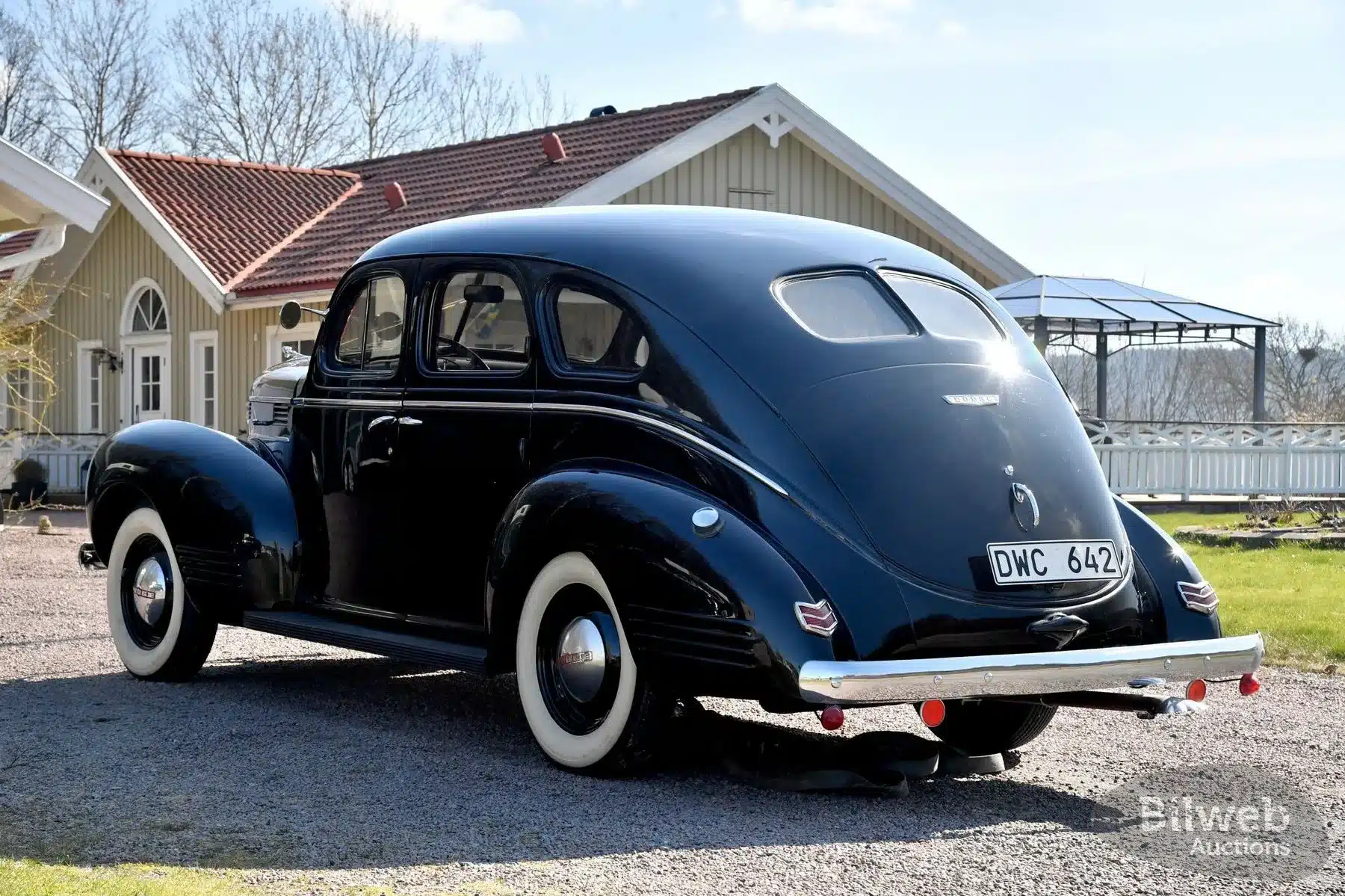 Dodge Senior Touring Sedan von 1939 in schwarzer Lackierung, geparkt auf einem Hof, Rückansicht mit weißwandbereiften Rädern und typischer Fastback-Karosserie.