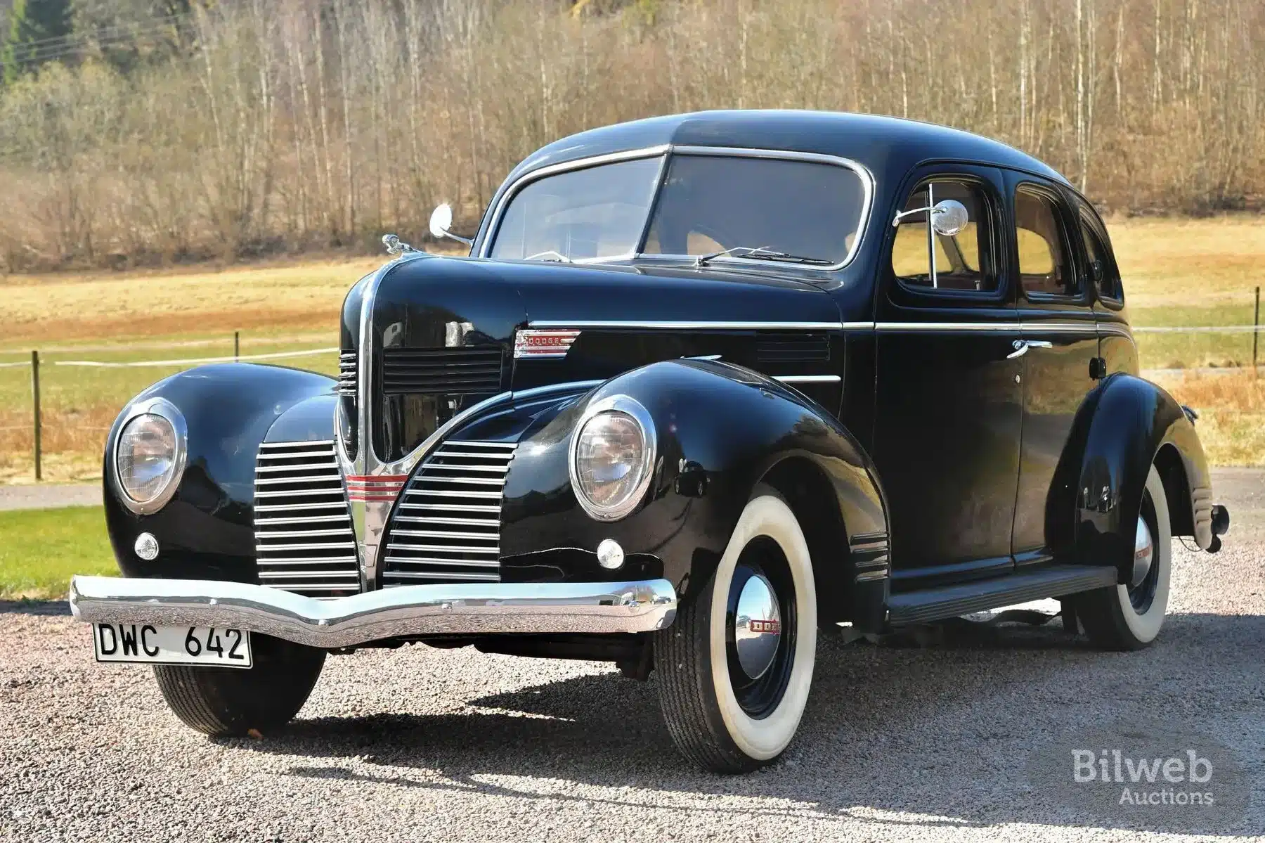 Schwarzer Dodge Senior Touring Sedan von 1939 mit weißwandreifen, stehend auf einem Kiesweg in ländlicher Umgebung.
