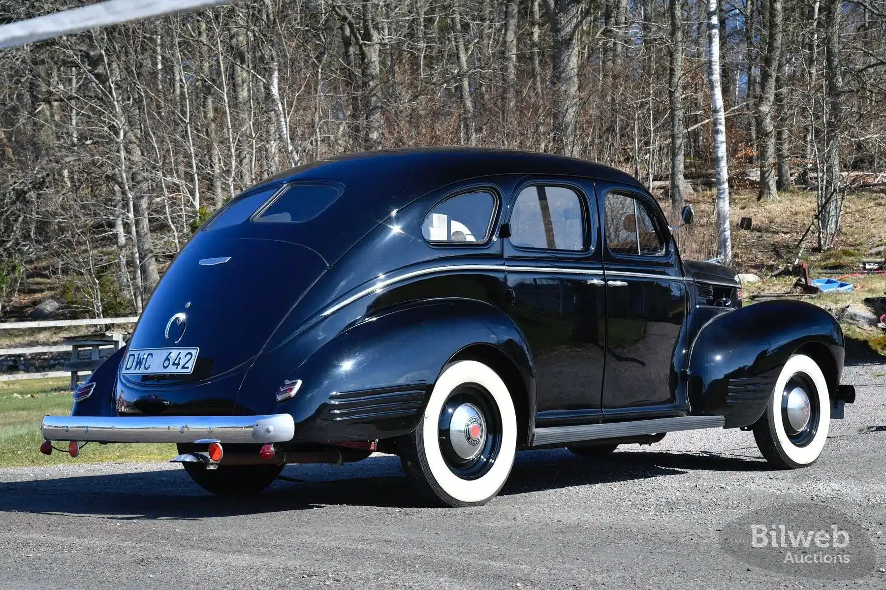 Dodge Senior Touring Sedan von 1939 in dunkler Lackierung, Seiten- und Heckansicht vor bewaldeter Kulisse, weißwandbereifte Räder.
