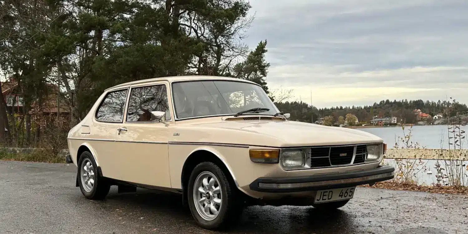 Saab 99 GL, Baujahr 1976, in beige auf einem Parkplatz vor herbstlicher Kulisse.