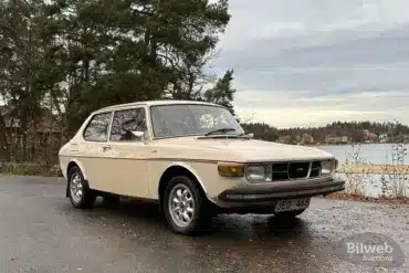 Saab 99 GL, Baujahr 1976, in beige auf einem Parkplatz vor herbstlicher Kulisse.