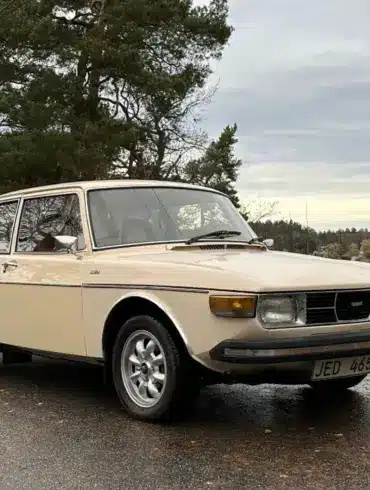 Saab 99 GL, Baujahr 1976, in beige auf einem Parkplatz vor herbstlicher Kulisse.