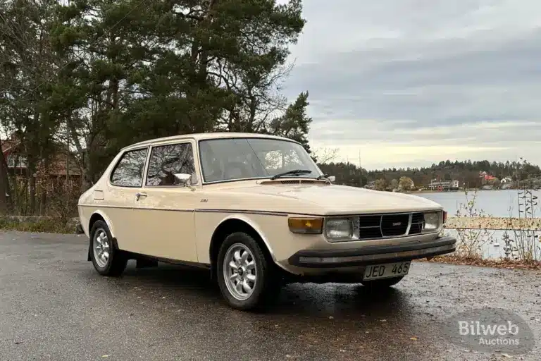 Saab 99 GL, Baujahr 1976, in beige auf einem Parkplatz vor herbstlicher Kulisse.