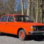 Hellroter Volvo 244 B20 Baujahr 1975 als klassische viertürige Limousine im Originalzustand, fotografiert im Freien vor schwedischer Waldkulisse.