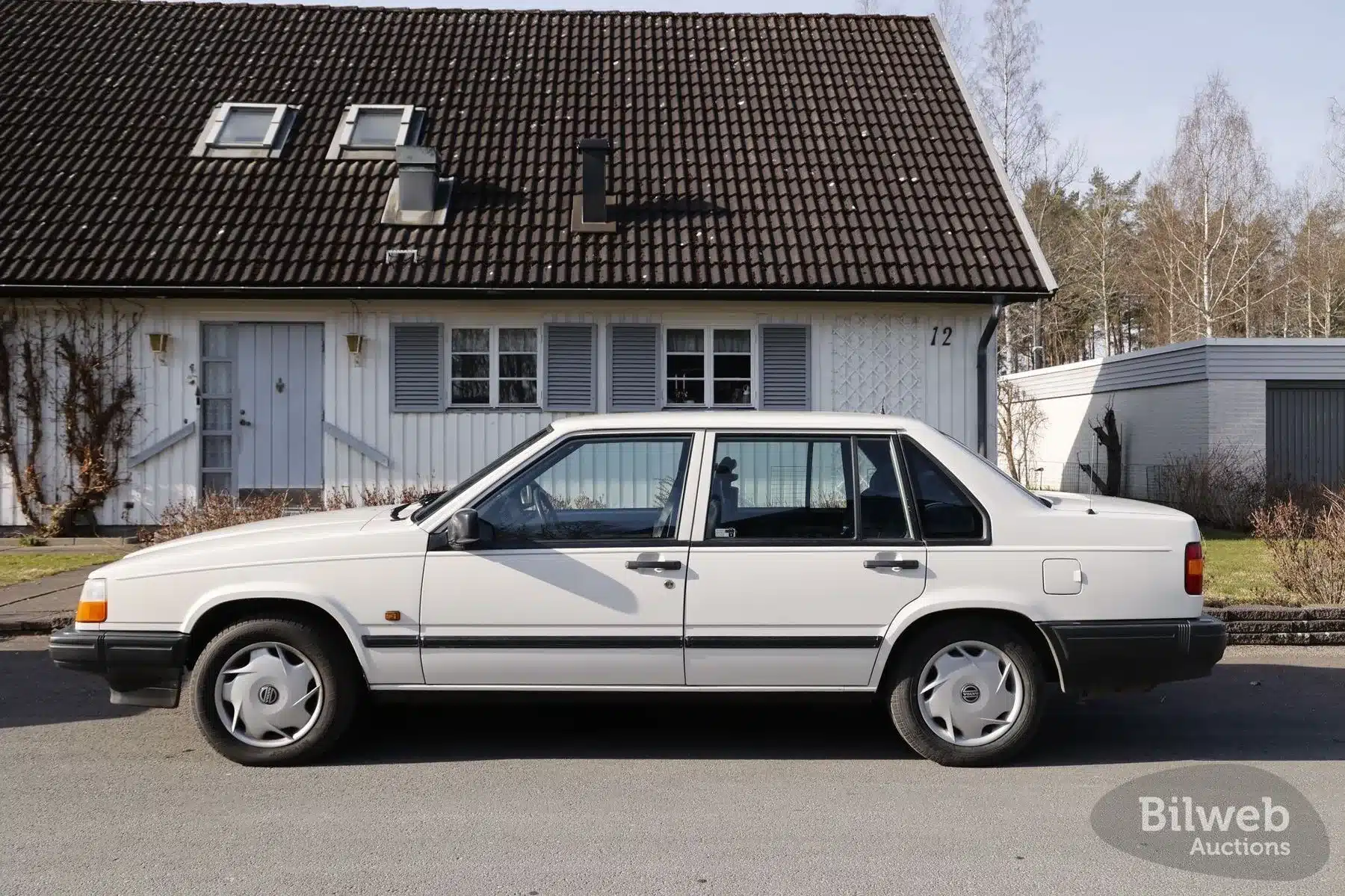 Weißer Volvo 940 Limousine Baujahr 1990 seitlich vor einem Haus geparkt