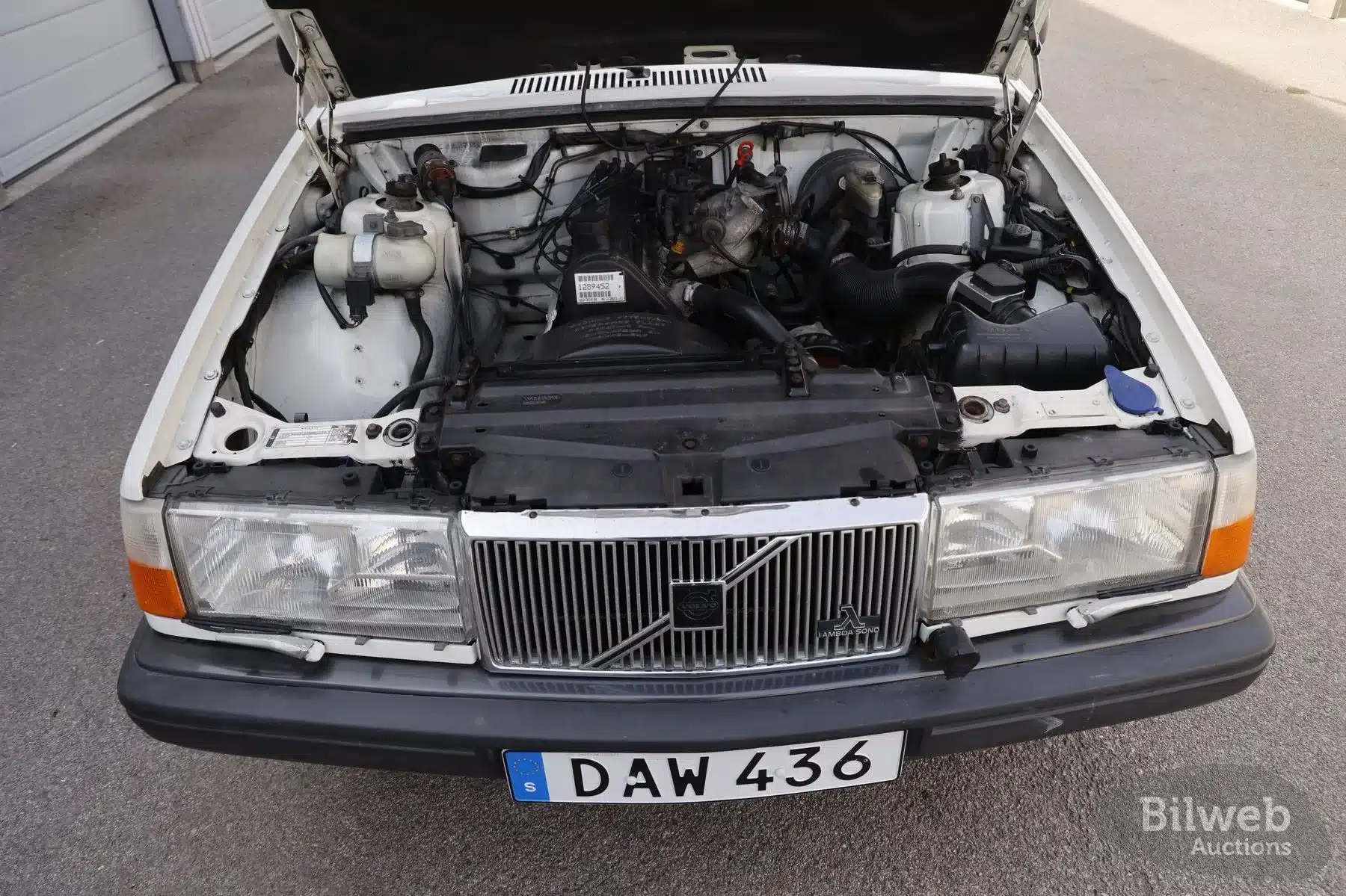 Geöffneter Motorraum eines weißen Volvo 940 aus dem Baujahr 1990 mit sichtbarem B230 Motor.