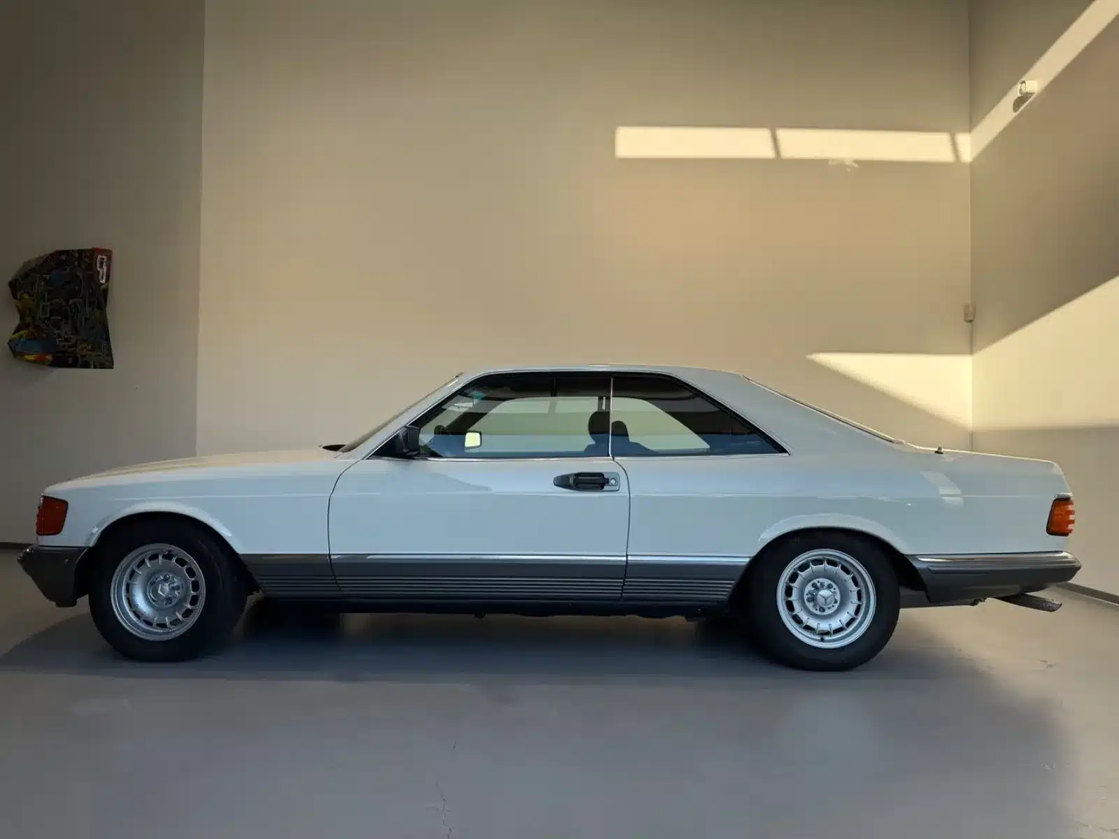 Weißer Mercedes-Benz 500 SEC Coupé, Baujahr 1980er, Seitenansicht in lichtdurchfluteter Garage