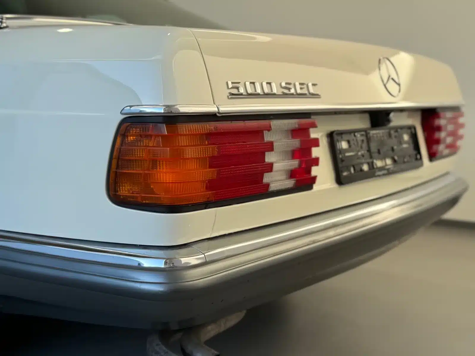 Heckpartie eines weißen Mercedes-Benz 500 SEC mit Emblem und Rückleuchten.