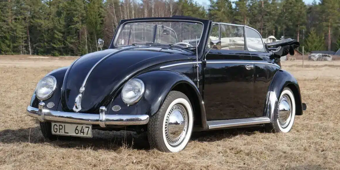 Frontansicht eines restaurierten schwarzen Volkswagen Käfer Cabriolets 1200 Baujahr 1956, mit geöffnetem Verdeck auf einer Wiese stehend.
