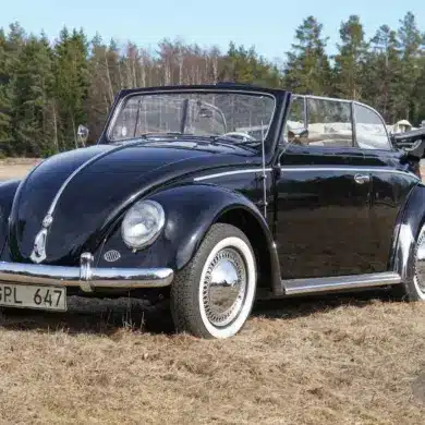 Frontansicht eines restaurierten schwarzen Volkswagen Käfer Cabriolets 1200 Baujahr 1956, mit geöffnetem Verdeck auf einer Wiese stehend.