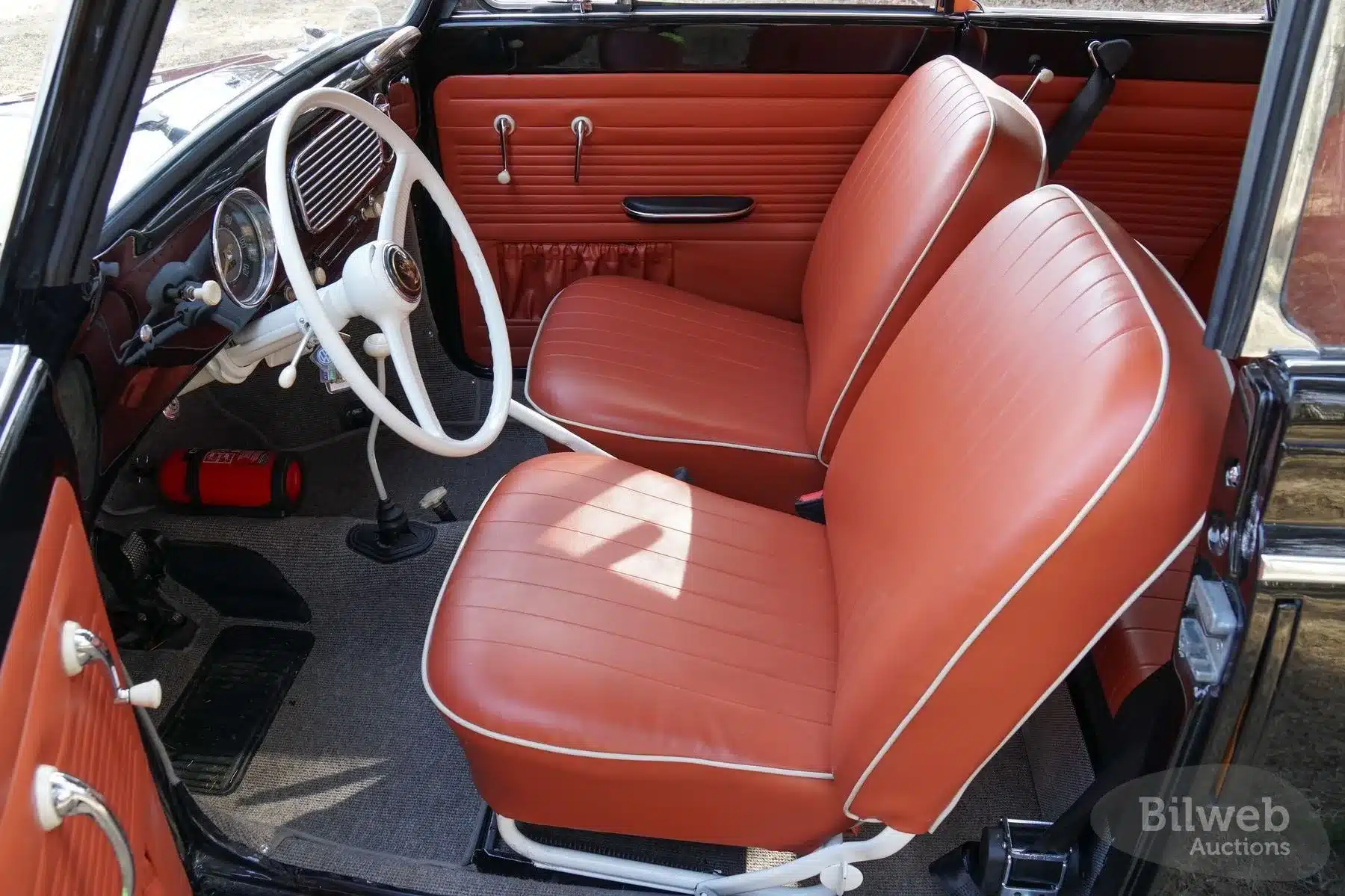 Detailaufnahme des roten Innenraums im Volkswagen Käfer 1200 Cabriolet von 1956 mit Lenkrad und Vordersitzen.