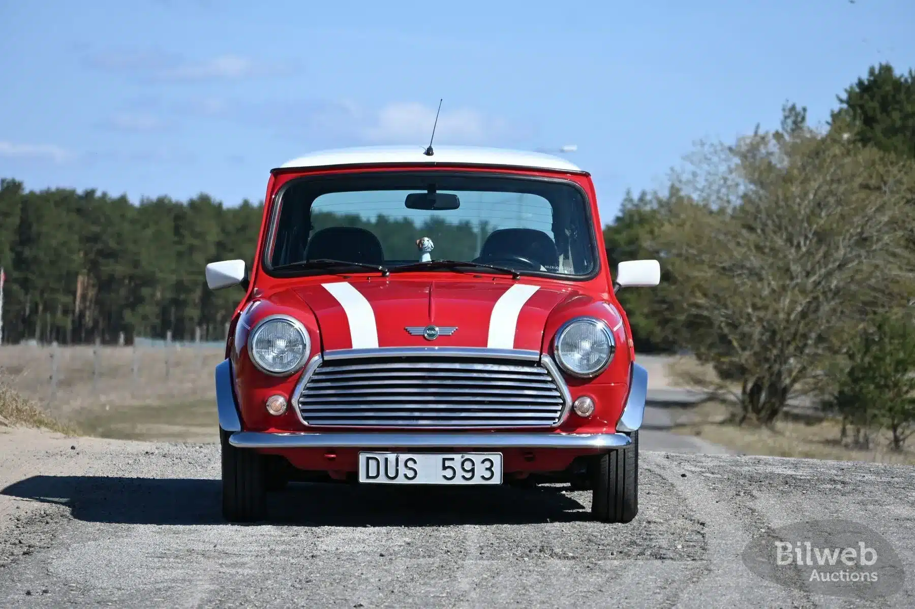 Roter Rover Mini Cooper 1997 von vorne auf einer Straße, typisches Modell mit weißen Streifen und weißem Dach