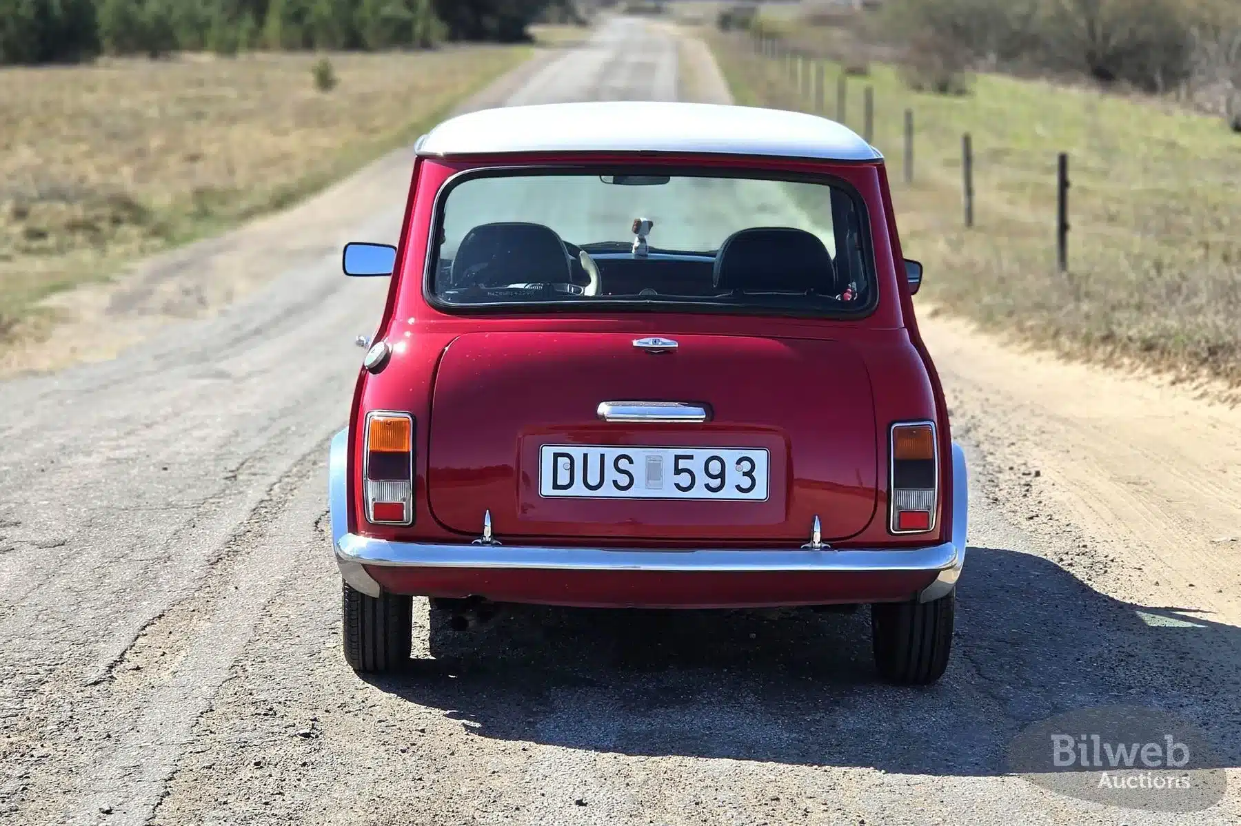 Roter Rover Mini Cooper 1997 mit weißem Dach von hinten auf einer Landstraße, schwedisches Kennzeichen.