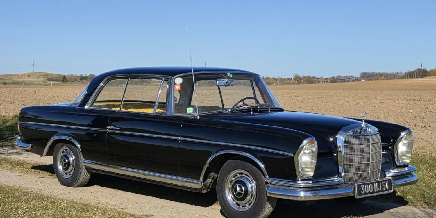 Schwarzes Mercedes-Benz 300 SE Coupé der Baureihe W112, Baujahr 1964, auf einem Feldweg vor offenem Landschaftshintergrund