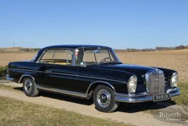 Schwarzes Mercedes-Benz 300 SE Coupé der Baureihe W112, Baujahr 1964, auf einem Feldweg vor offenem Landschaftshintergrund