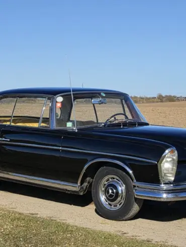 Schwarzes Mercedes-Benz 300 SE Coupé der Baureihe W112, Baujahr 1964, auf einem Feldweg vor offenem Landschaftshintergrund