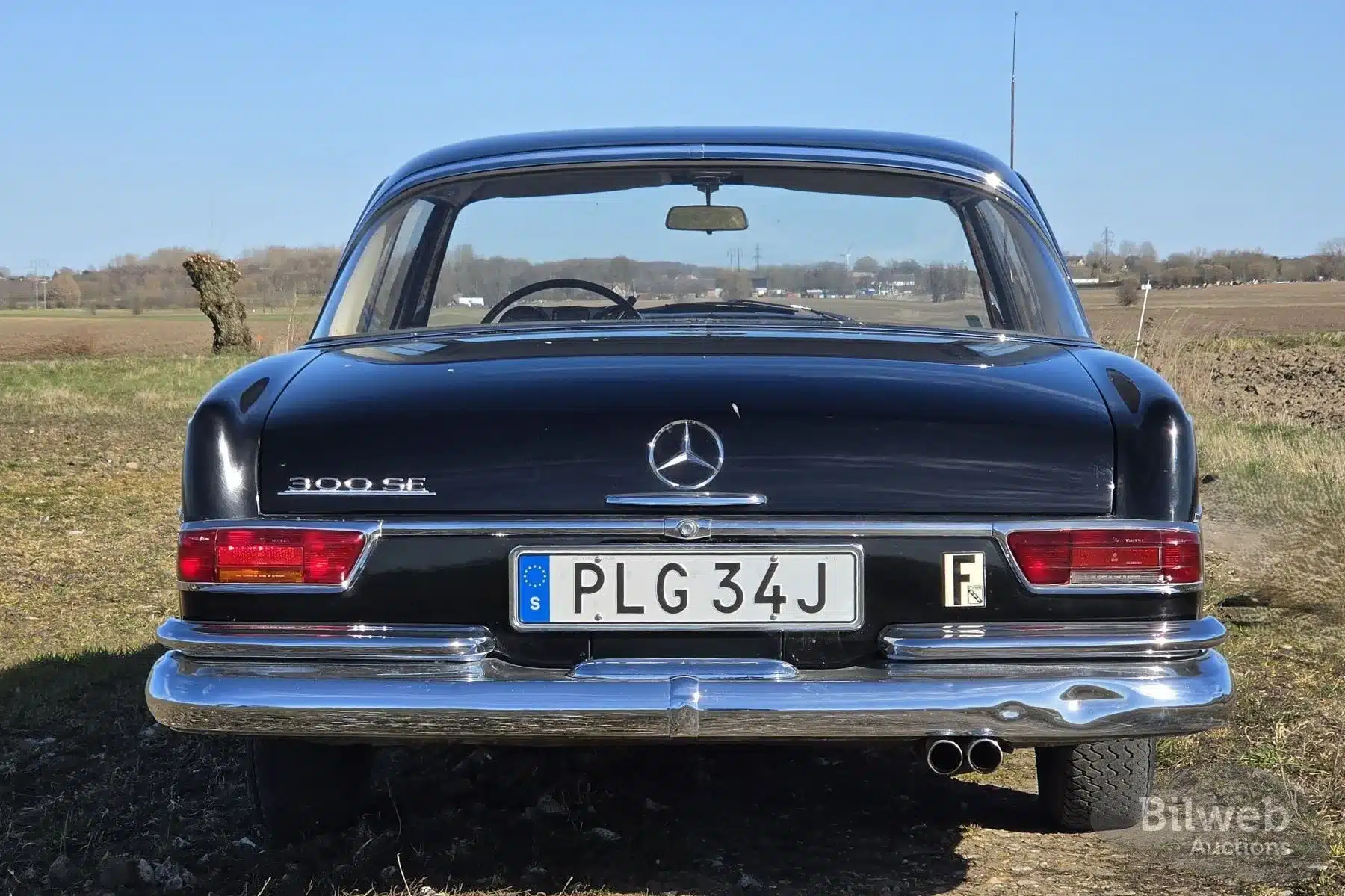 Heckansicht eines schwarzen Mercedes-Benz 300 SE Coupé der Baureihe W112 auf einer Landstraße, Baujahr 1964.