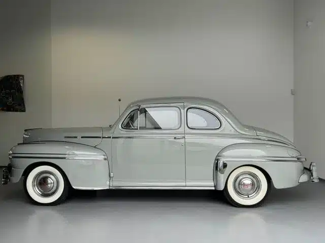 Seitenansicht eines silbergrauen Mercury Eight V8 Coupés mit weißwandreifen in einem hellen Raum