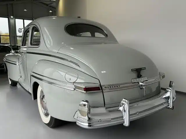 Heckansicht eines Mercury Eight V8 Oldtimers in hellgrau mit viel Chrom in einer Halle.