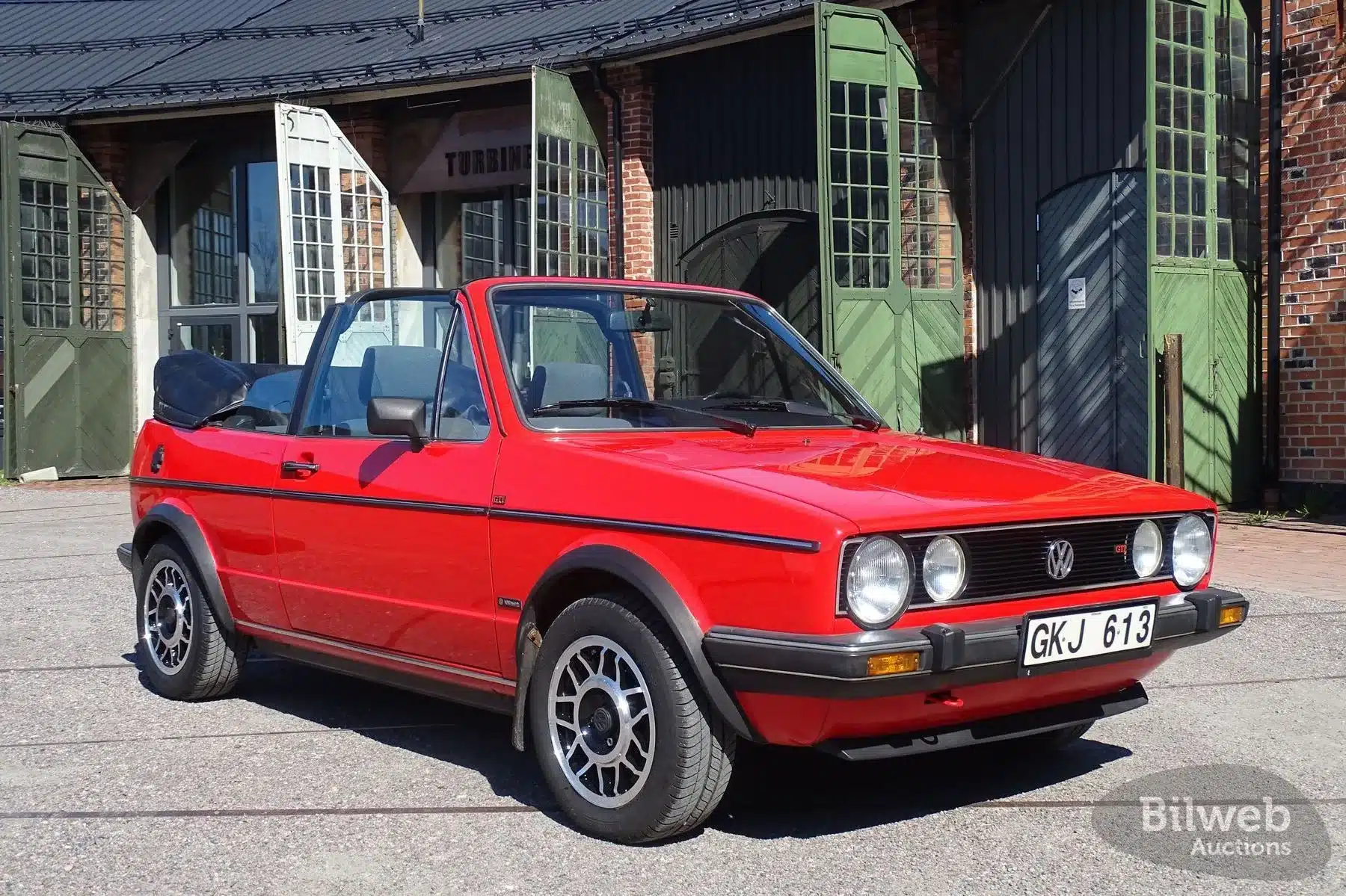 VW Golf Cabriolet 1.8 GLI, Baujahr 1985, marsrot mit schwarzem Stoffverdeck, vor Industriegebäude, Seitenansicht, Sonnenlicht
