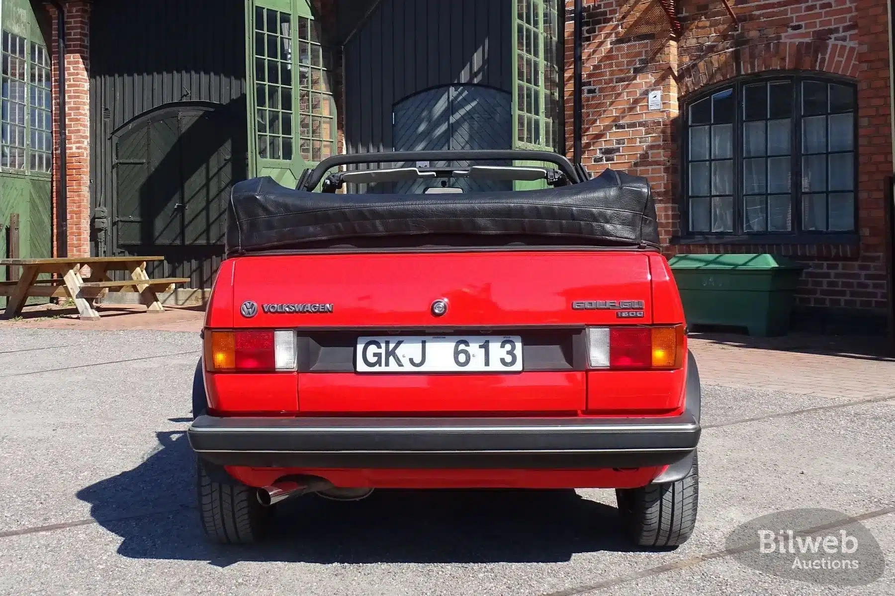 Heckansicht eines roten VW Golf Cabriolet 1.8 GLI Baujahr 1985 mit Stoffverdeck, aufgenommen bei Tageslicht vor einer Backsteinhalle.