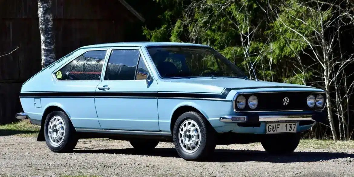 Hellblauer VW Passat TS 1500 von 1974 in Seitenansicht, mit Doppelscheinwerfern und Chromstoßstangen, aufgenommen vor Waldkulisse.