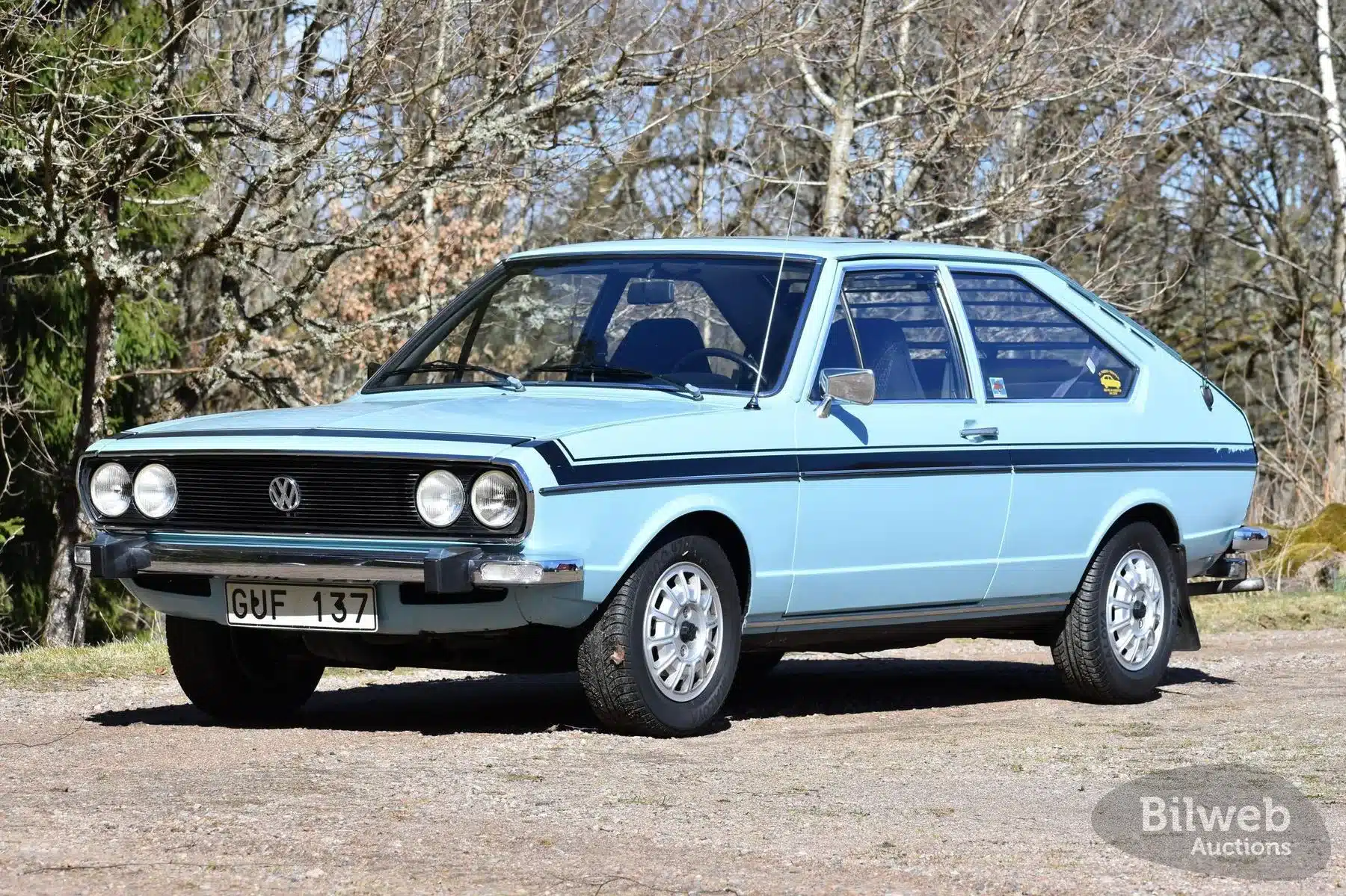 Originaler VW Passat TS 1500 von 1974 in hellblau, Seitenansicht mit Doppelscheinwerfern und Chromstoßstange, abgestellt im Freien vor Bäumen.