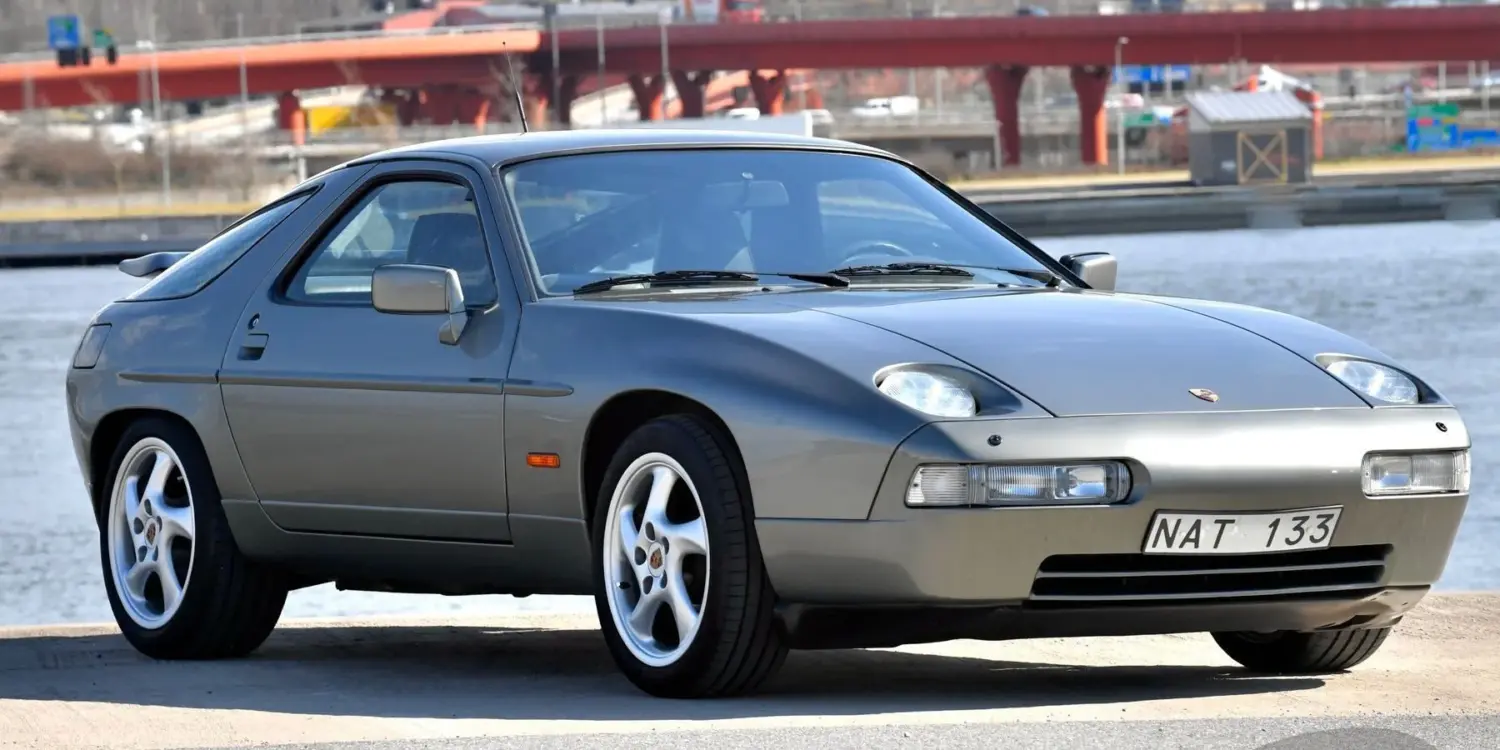 Originaler Porsche 928 S4 V8 von 1988 in silbergrauer Lackierung, seitlich vor urbaner Kulisse am Wasser abgestellt