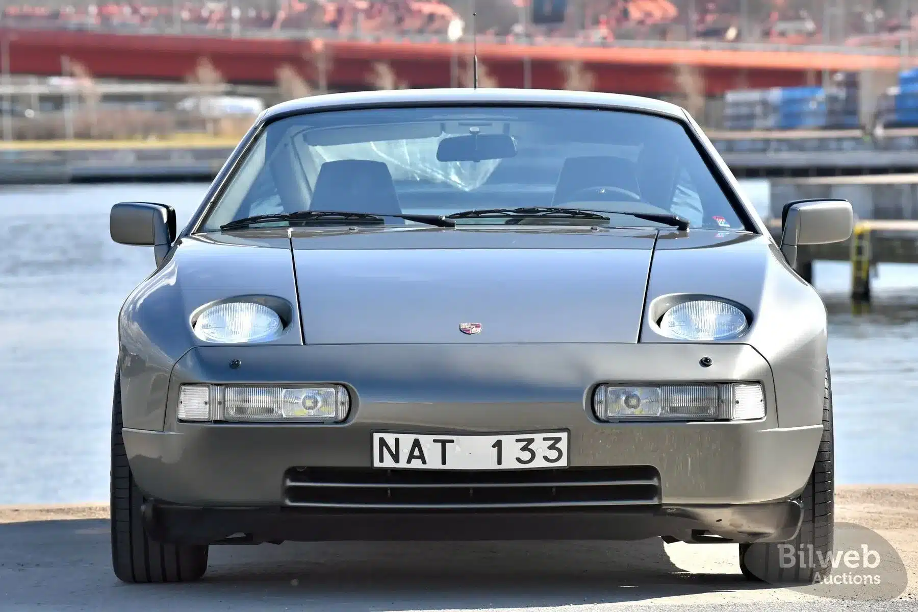 Porsche 928 S4 V8, Modelljahr 1988, in silbergrau, Frontansicht am Wasser.