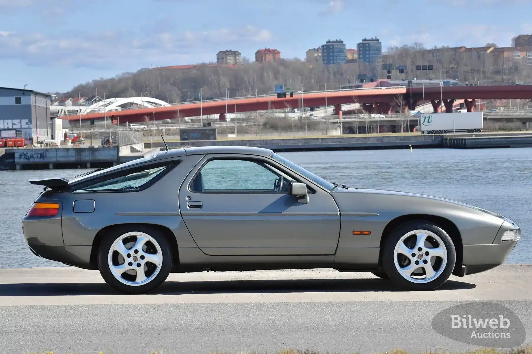 Porsche 928 S4 V8, Baujahr 1988, in seitlicher Ansicht vor einer Wasser- und Stadtlandschaft