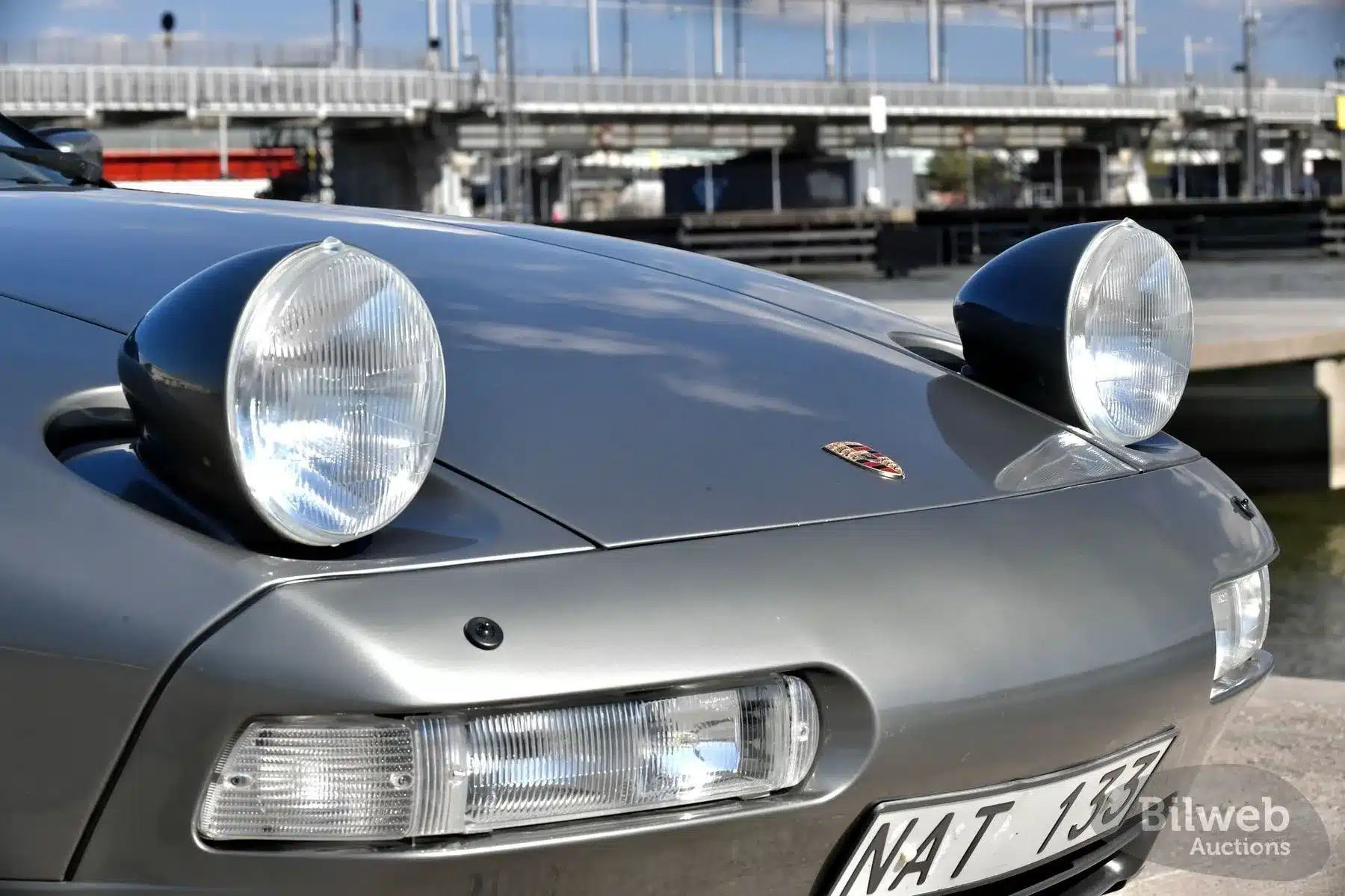 Porsche 928 S4 mit geöffneten Klappscheinwerfern, silber, Detailansicht der Frontpartie.
