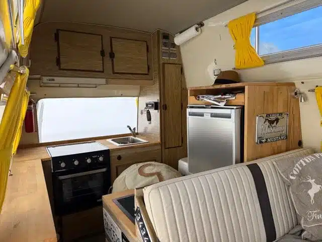 Innenansicht eines Ford Econoline Custom-Minihome-Campervans mit Küchenzeile, Sitzbank und gelben Vorhängen.