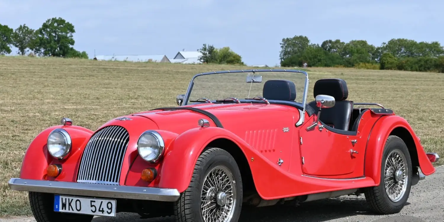 Roter Morgan 4/4 Roadster von 1998 mit Speichenrädern und schwarzem Interieur, fotografiert auf einer Landstraße.