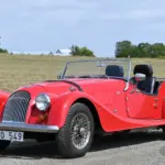 Roter Morgan 4/4 Roadster von 1998 mit Speichenrädern und schwarzem Interieur, fotografiert auf einer Landstraße.