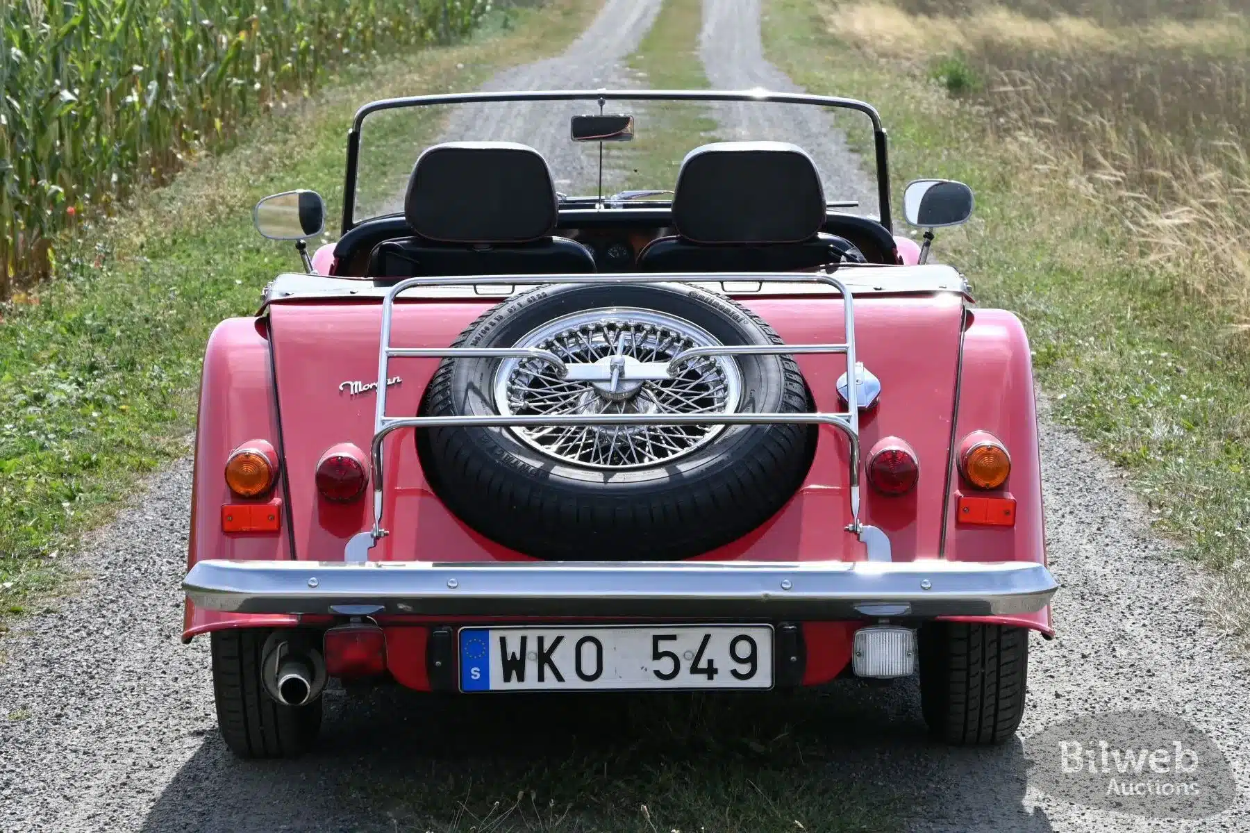Heckansicht eines roten Morgan 4/4 Roadsters von 1998 mit montiertem Reserverad auf einer Schotterstraße