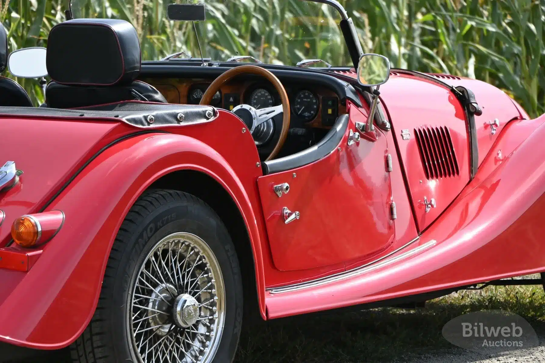 Roter Morgan 4/4 Roadster von 1998 mit klassischem Holzlenkrad und Speichenrädern, Verdeck und Innenraum im Fokus