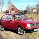 Volvo 142 B20 von 1969 in Rot, stehend auf einem ländlichen Weg vor Scheune.