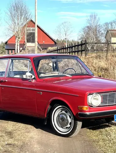 Volvo 142 B20 von 1969 in Rot, stehend auf einem ländlichen Weg vor Scheune.