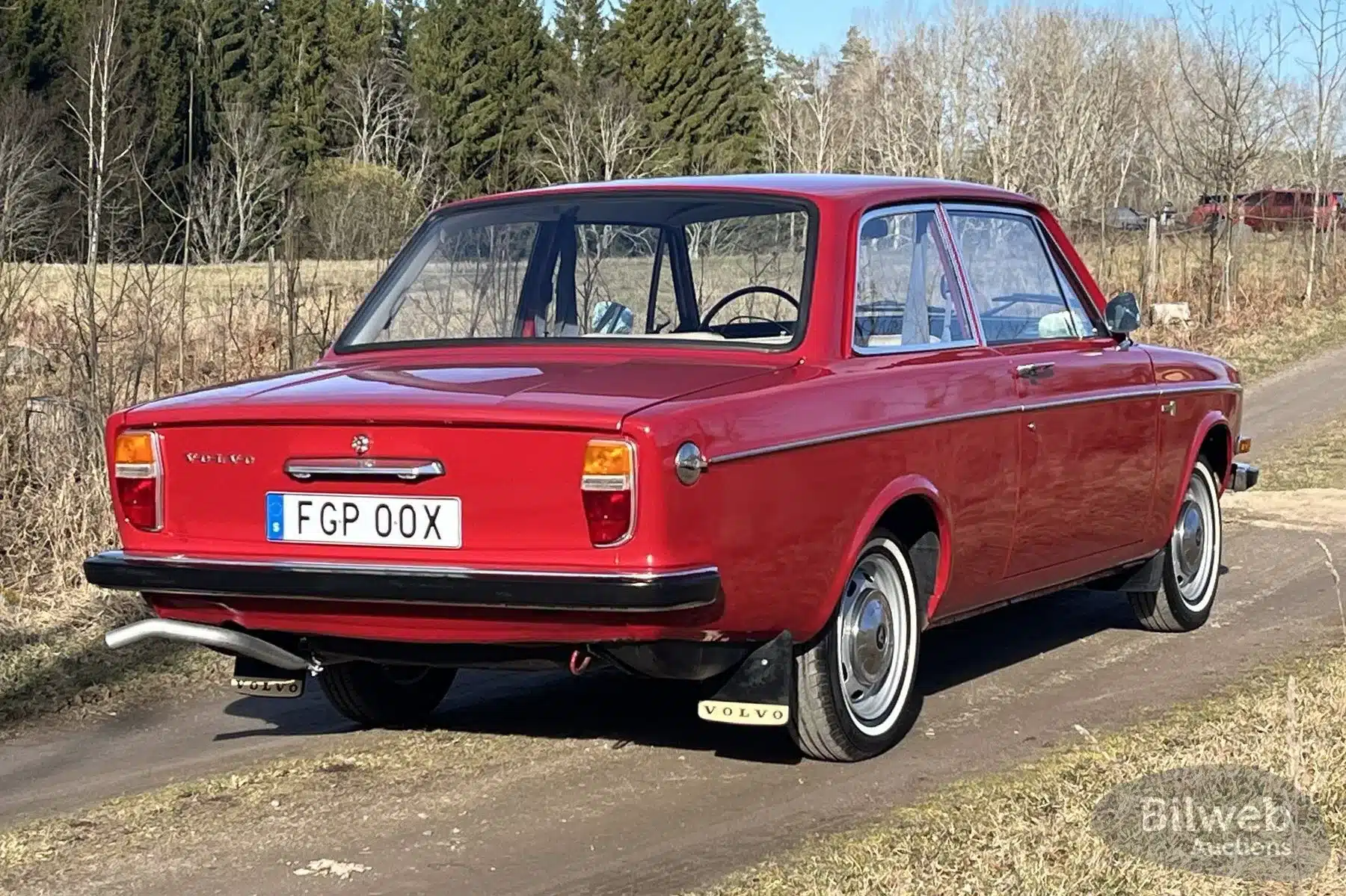 Heckansicht eines roten Volvo 142 B20 von 1969 auf einem Feldweg, schwedisches Kennzeichen, originale Details sichtbar.