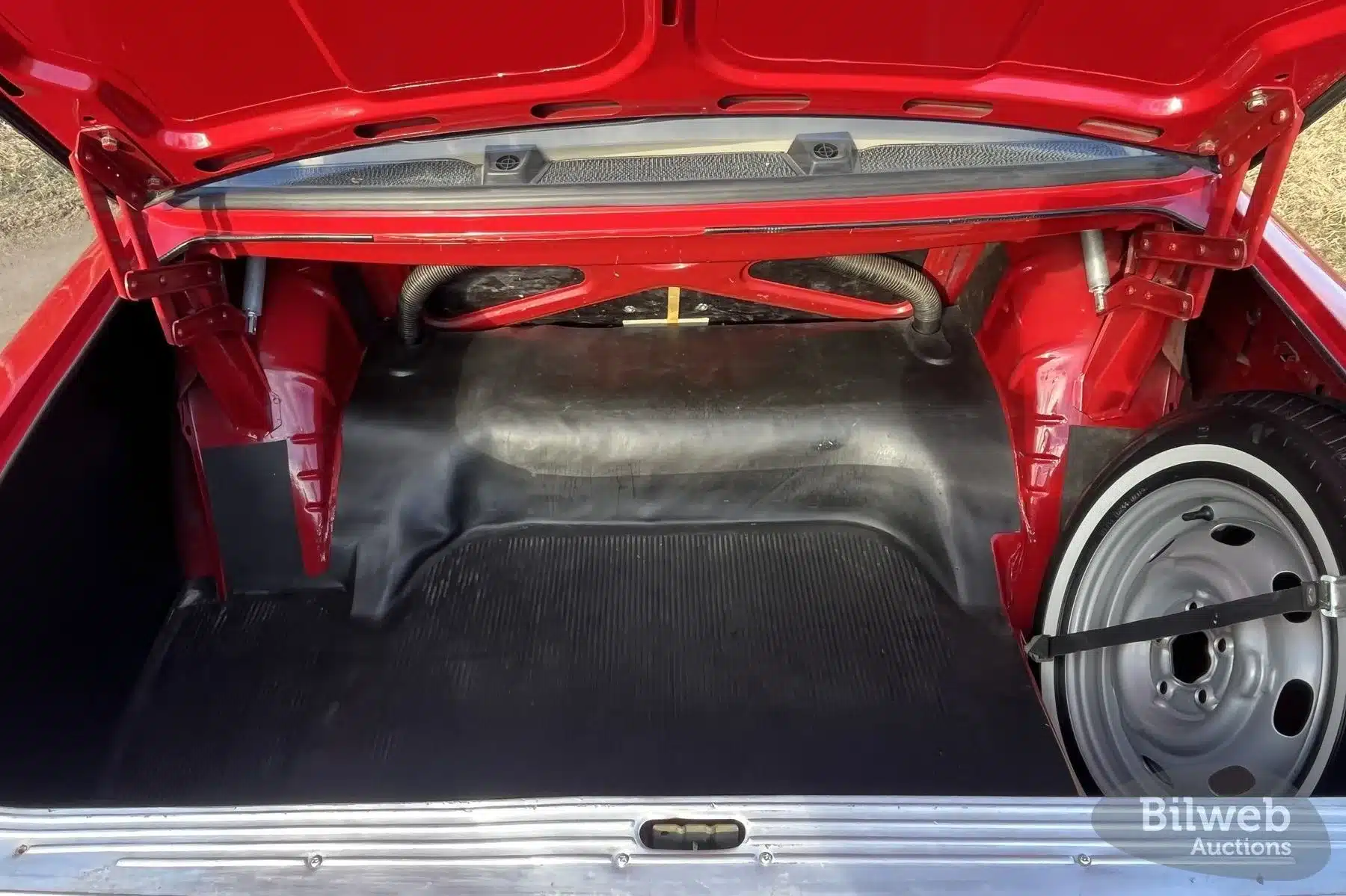 Blick in den offenen Kofferraum eines roten Volvo 142 B20 von 1969 mit sichtbarem Ersatzrad und gepflegter Innenausstattung.