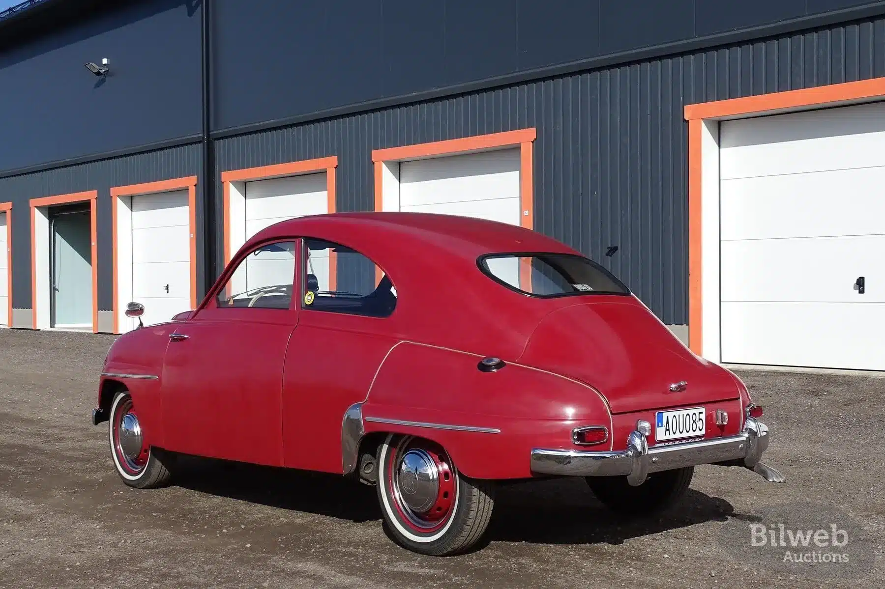 Roter Saab 93B von 1958 mit originaler Lackierung und altersbedingten Gebrauchsspuren, geparkt vor Garagen.
