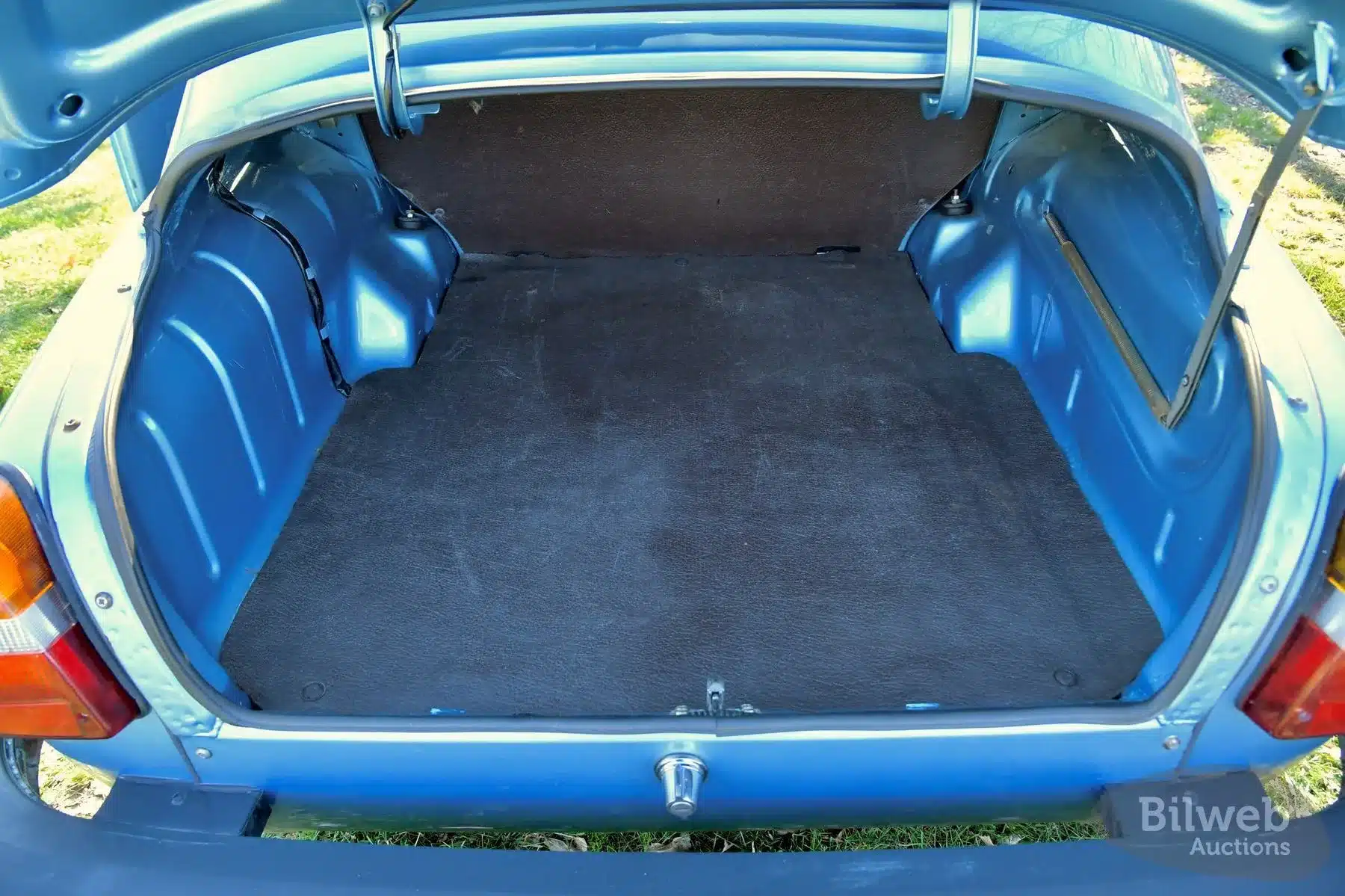 Offener Kofferraum eines Saab 96 Jubileum V4 von 1980, sauber und original erhalten, mit blau lackiertem Karosserieblech und schwarzem Teppichbelag.