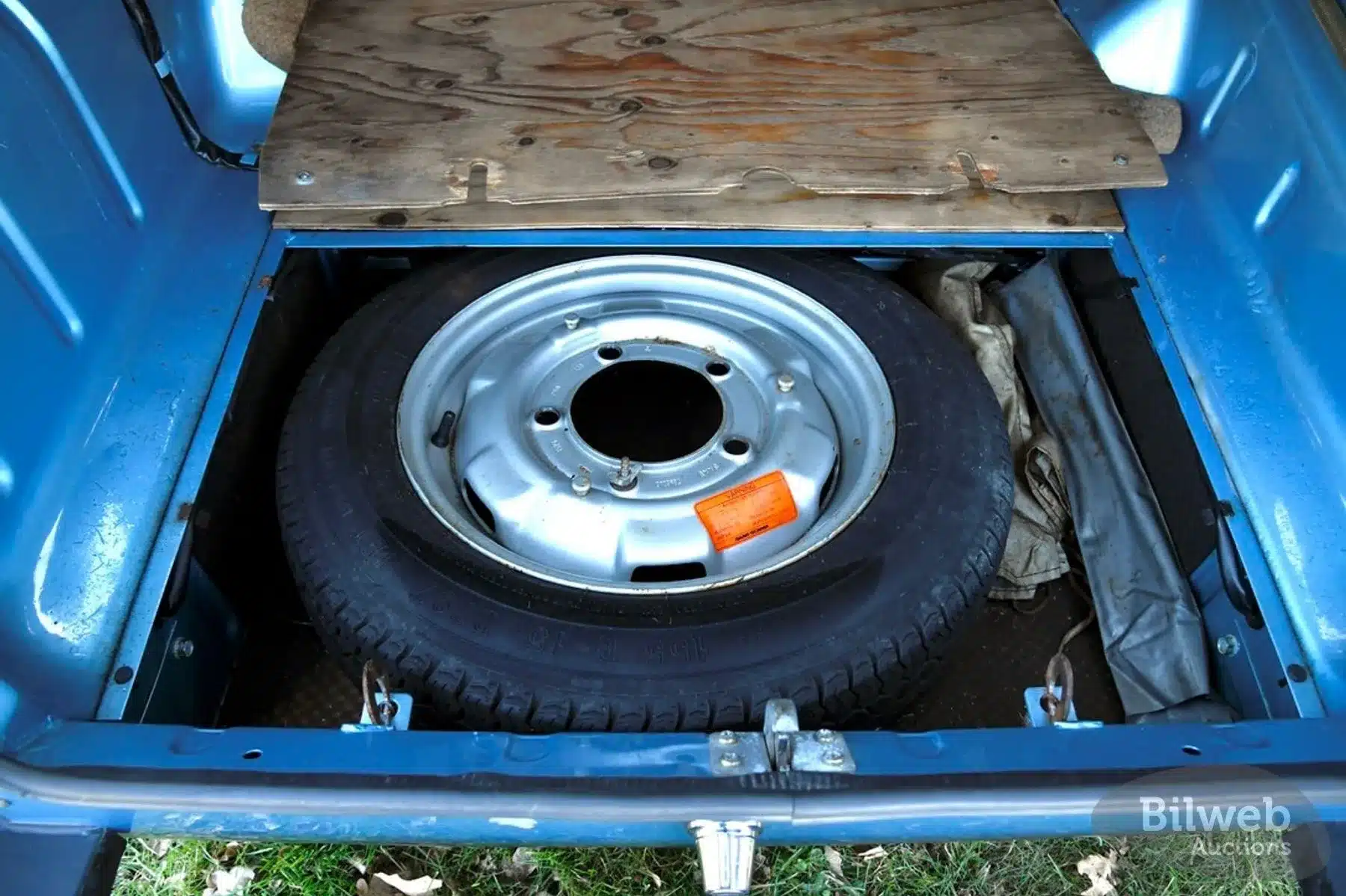 Reserverad im Kofferraum eines Saab 96 Jubileum V4 von 1980, unter einer Holzplatte verstaut.