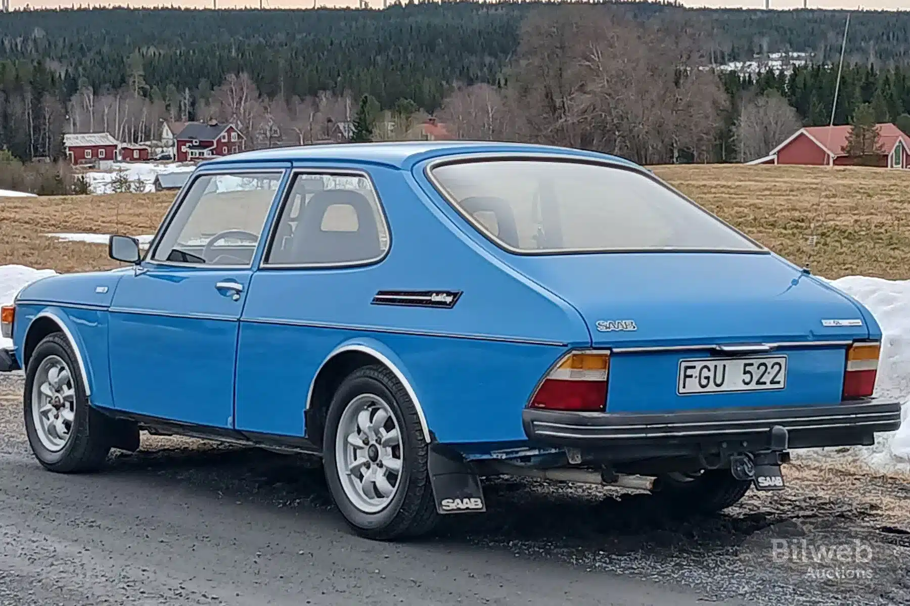 Blauer Saab 99 GL 2,0 von 1977 mit Minilite-Leichtmetallrädern auf einer Landstraße, fotografiert von hinten seitlich