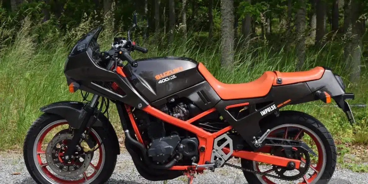 Seitliche Ansicht einer Suzuki GSX 400X Impulse von 1989 mit rotem Rahmen und schwarzem Tank, fotografiert vor grünem Waldhintergrund.