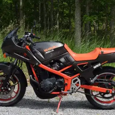 Seitliche Ansicht einer Suzuki GSX 400X Impulse von 1989 mit rotem Rahmen und schwarzem Tank, fotografiert vor grünem Waldhintergrund.