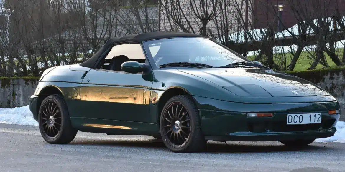 Lotus Elan 1.6 Turbo 16V aus dem Jahr 1991 in Dunkelgrün mit geschlossenem Verdeck und schwarzen Alufelgen, fotografiert im Freien.