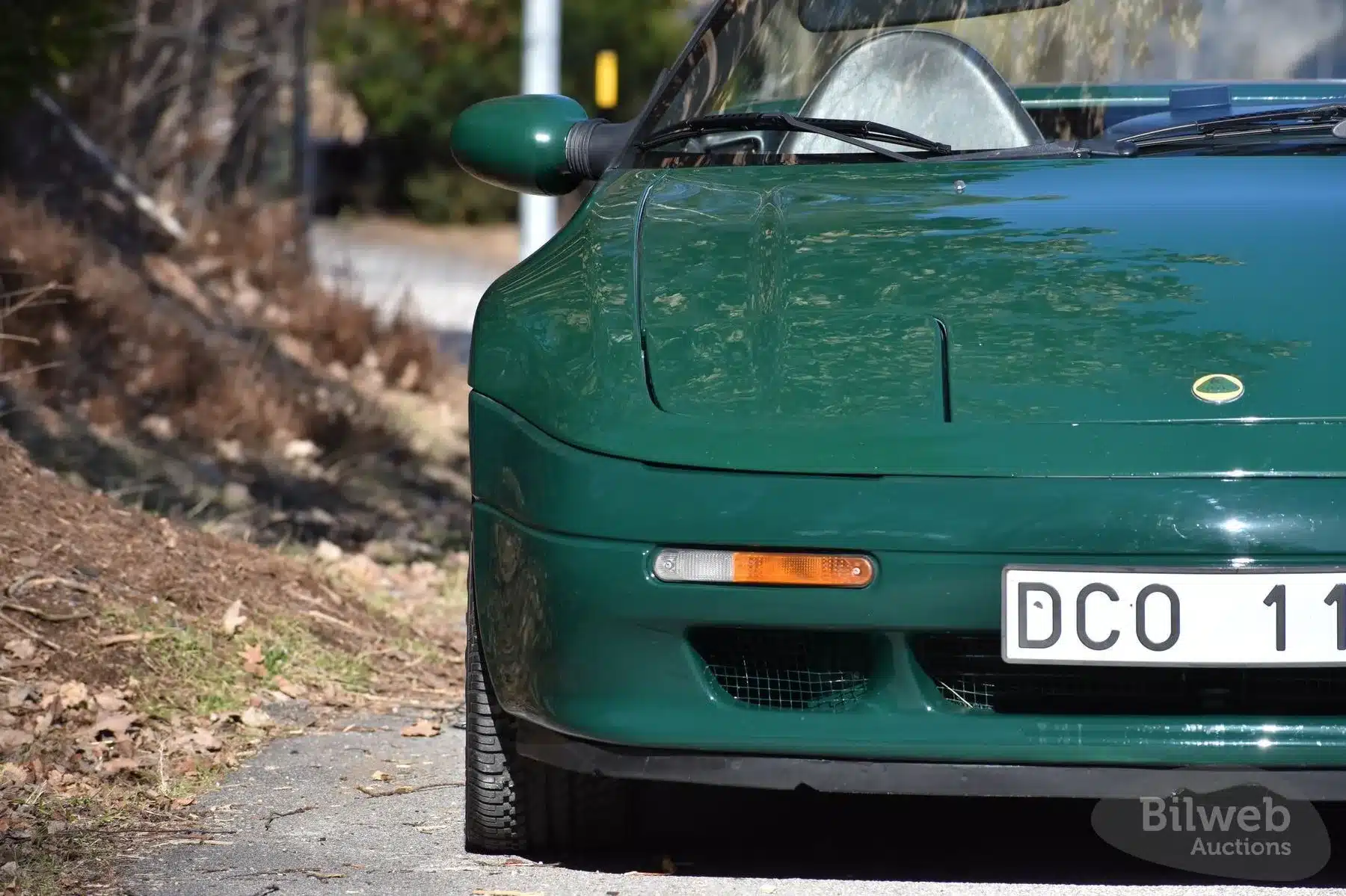 Grüner Lotus Elan M100 Turbo Cabriolet, Detailaufnahme der Frontpartie auf einer Straße, Teil des Fahrzeugs mit Scheinwerfer und schwedischem Kennzeichen.