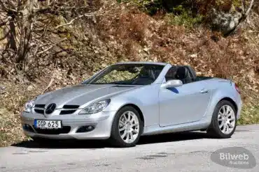 Silberner Mercedes-Benz SLK 280 (R171) mit geöffnetem Dach auf einer Straße vor herbstlicher Kulisse.