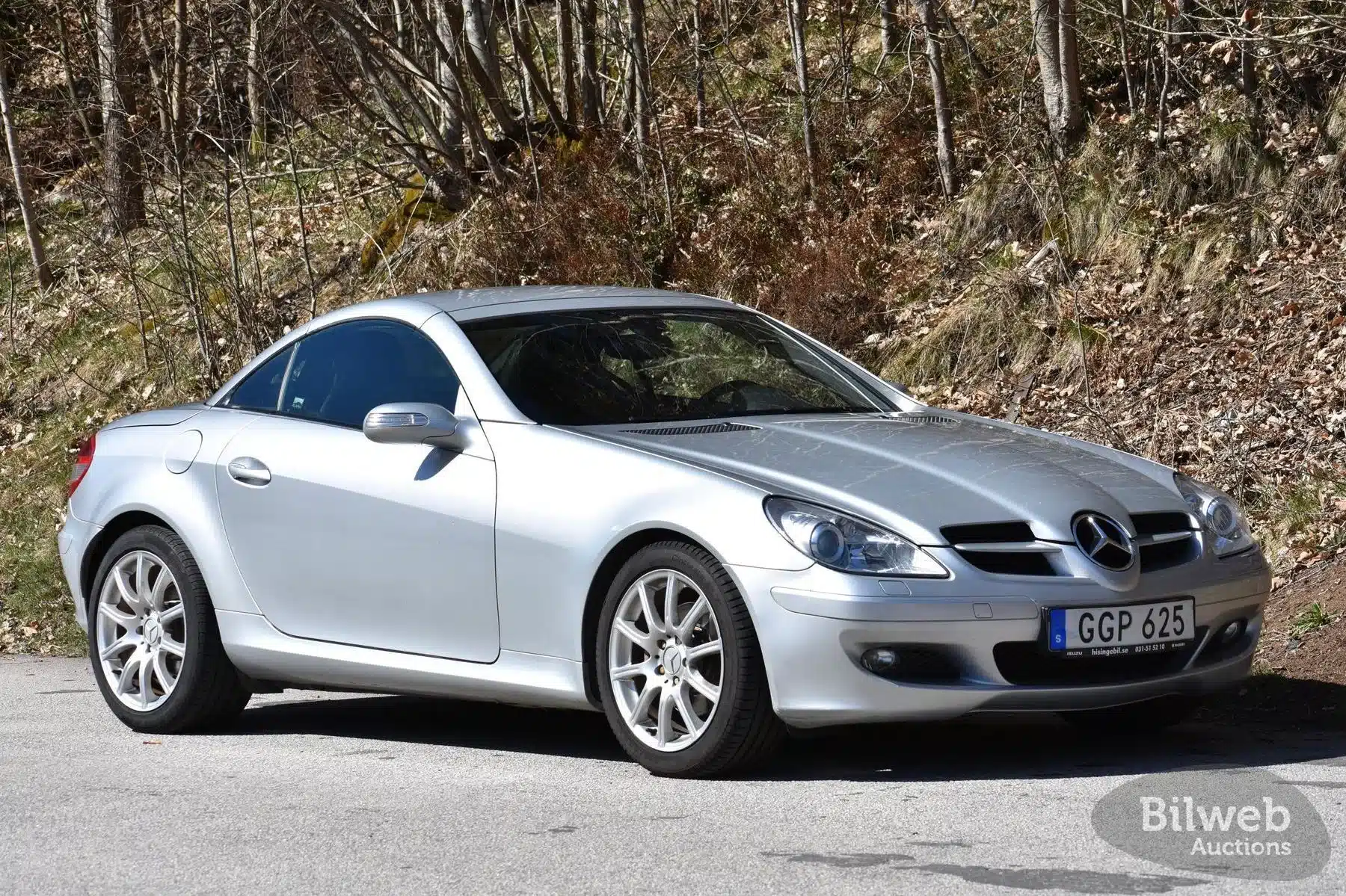 Silberner Mercedes-Benz SLK 280 (R171) mit geschlossenem Dach im Profil auf einer Straße in Waldumgebung.